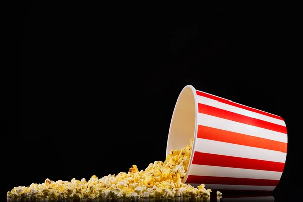 Scattered popcorn from paper striped bucket isolated on black background — Stock Photo, Image