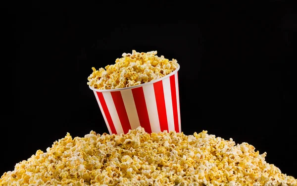 Cubo de rayas de papel instalado sobre palomitas dispersas aisladas sobre fondo negro — Foto de Stock