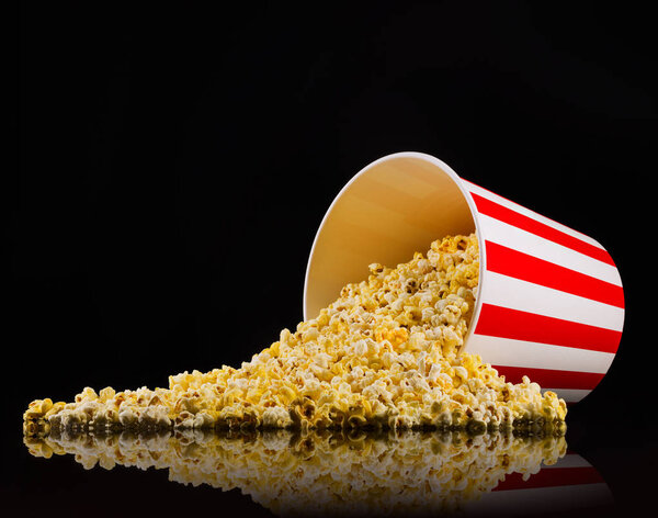 Scattered popcorn from paper striped bucket isolated on black background