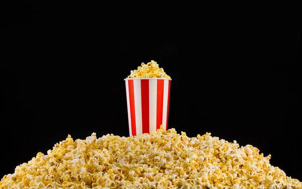 Paper striped bucket installed on scattered popcorn isolated on black background — Stock Photo, Image