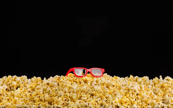 Okulary kinowe zainstalowane na rozproszonym popcorn na czarnym tle — Zdjęcie stockowe