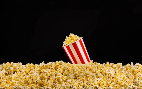 Papiergestreifter Eimer auf verstreutem Popcorn isoliert auf schwarzem Hintergrund installiert — Stockfoto