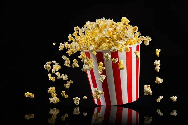 Fliegendes Popcorn aus gestreiftem Eimer isoliert auf schwarzem Hintergrund — Stockfoto