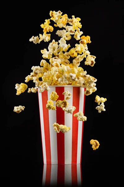 Fliegendes Popcorn aus gestreiftem Eimer isoliert auf schwarzem Hintergrund — Stockfoto