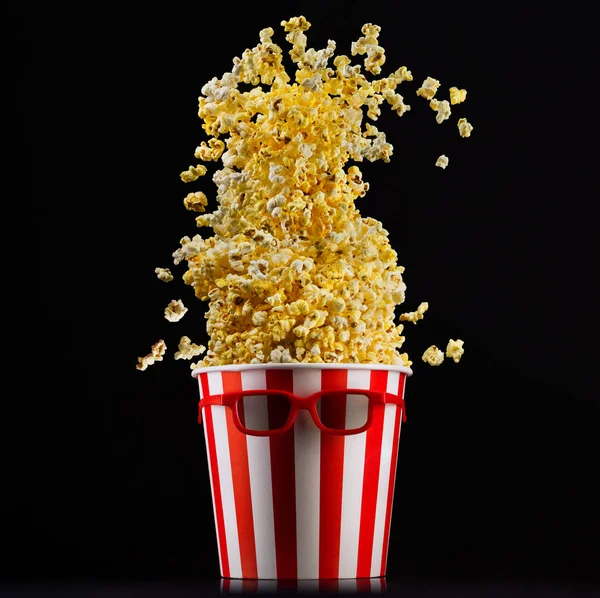 Fliegendes Popcorn aus gestreiftem Eimer isoliert und 3D-Gläser auf schwarzem Hintergrund — Stockfoto