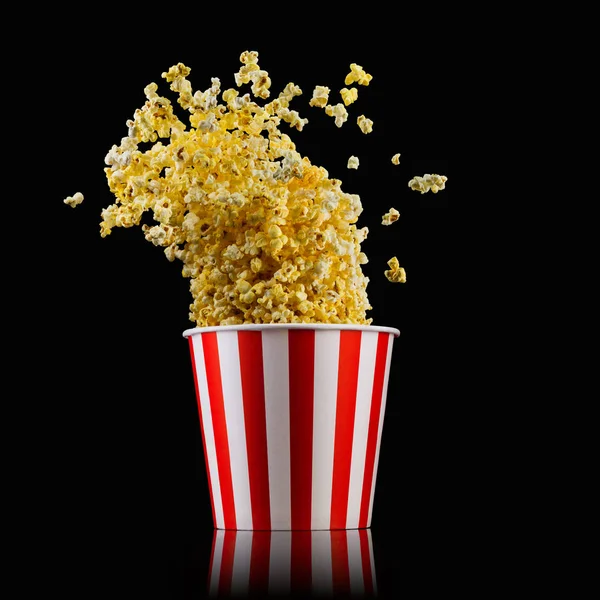 Fliegendes Popcorn aus gestreiftem Eimer isoliert auf schwarzem Hintergrund — Stockfoto