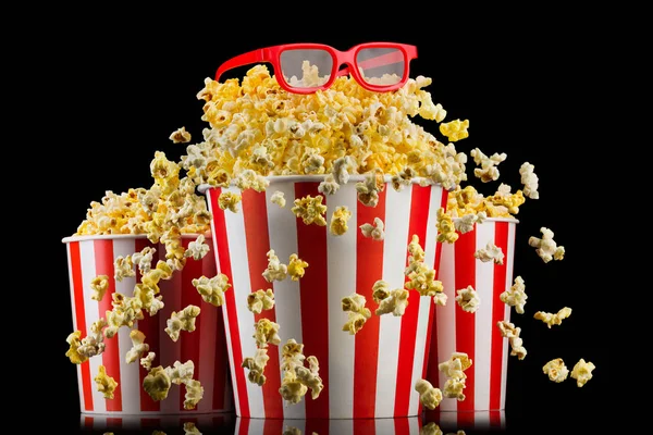 Papiereimer mit Popcorn und Gläsern isoliert auf schwarzem Hintergrund — Stockfoto
