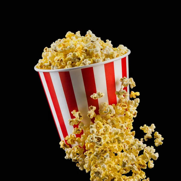 Fliegendes Popcorn aus gestreiftem Eimer isoliert auf schwarzem Hintergrund — Stockfoto