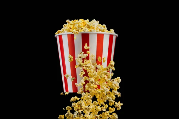 Fliegendes Popcorn aus gestreiftem Eimer isoliert auf schwarzem Hintergrund — Stockfoto