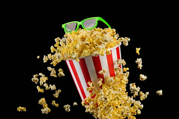 Fliegendes Popcorn aus gestreiftem Eimer isoliert auf schwarzem Hintergrund — Stockfoto