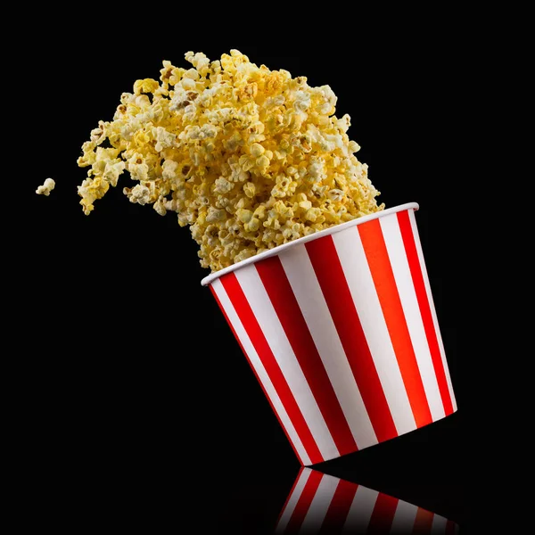 Fliegendes Popcorn aus gestreiftem Eimer isoliert auf schwarzem Hintergrund — Stockfoto