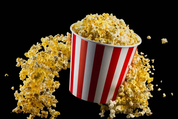 Fliegendes Popcorn aus gestreiftem Eimer isoliert auf schwarzem Hintergrund — Stockfoto