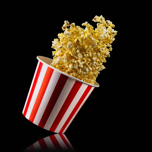 Fliegendes Popcorn aus gestreiftem Eimer isoliert auf schwarzem Hintergrund — Stockfoto