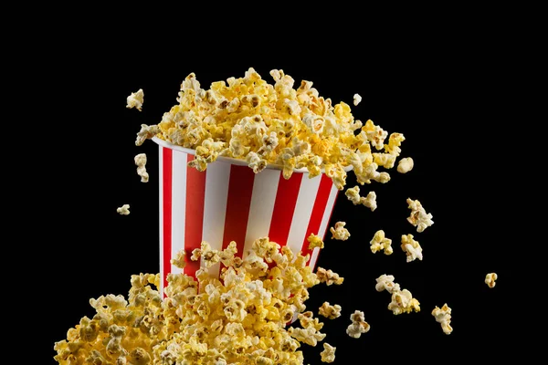 Vliegende popcorn uit gestreepte emmer geïsoleerd op zwarte achtergrond — Stockfoto
