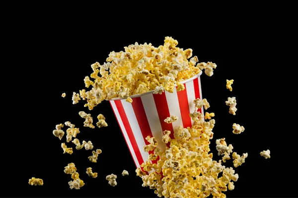 Fliegendes Popcorn aus gestreiftem Eimer isoliert auf schwarzem Hintergrund — Stockfoto