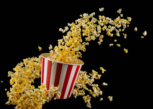 Fliegendes Popcorn aus gestreiftem Eimer isoliert auf schwarzem Hintergrund — Stockfoto