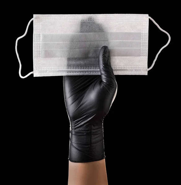 Mano in guanti neri tenendo maschera monouso isolato su sfondo nero — Foto Stock