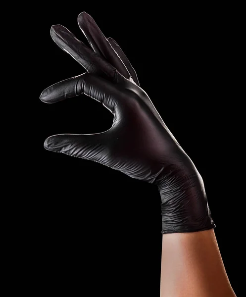 Mão em luvas pretas segurando algo com dois dedos isolados em preto — Fotografia de Stock