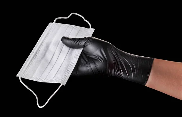 Χέρι σε μαύρα γάντια που κρατούν μάσκα προσώπου μίας χρήσης απομονωμένη σε μαύρο φόντο — Φωτογραφία Αρχείου