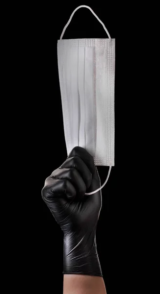 Mão em luvas pretas segurando máscara facial descartável isolado em fundo preto — Fotografia de Stock