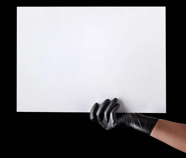 Χέρι σε μαύρα γάντια κρατώντας λευκό χαρτόνι απομονώνονται σε μαύρο — Φωτογραφία Αρχείου
