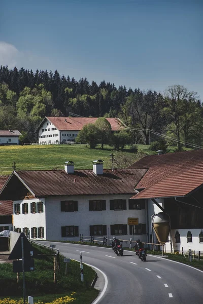İki motosikletli otoyolda giderken yeşil tarlaların arka planında kırsal evleri, güneşli yaz günlerinde orman ve mavi gökyüzü olan Alp köyü atıyorlar. Dikey duvar kağıdı
