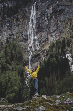 Schonau am Konigssee. Bavyera 'da. Almanya. Sarı kazaklı genç beyaz kız ellerini kaldırdı ve Rothbach şelalesinin arka planında özgürlüğü hissetti.
