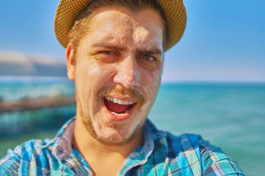 Çocukla koruması losyon yüzünde bir selfie alarak veya canlı video akışı yapma. Adam tatilde ve güneş kremi ile bulaşmış ve elinde tutuyor.