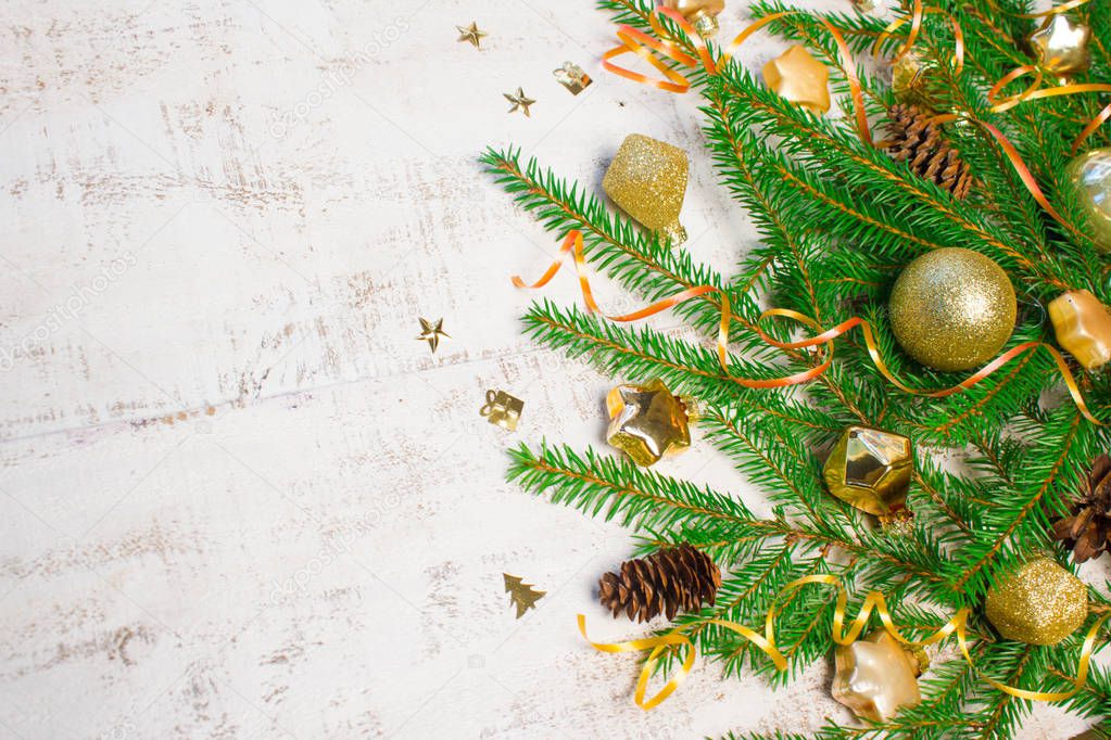 Christmas or New Year background: fir tree branches, gold glass toys, decorations and cones on a white wooden background.