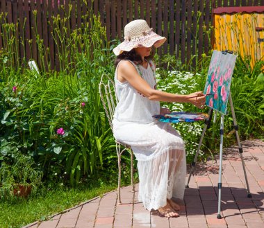 beyaz şapka ve elbise boyama gül genç kadın bahçede otururken 