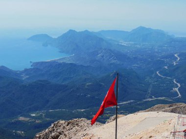           Türk bayrağı sisli deniz kıyısının arka planına karşı Tahtali Dağı 'nda dalgalanıyor. Akdeniz 'in manzarası. Olympos Teleferik, Tahtali 2365 metre, Kemer, Antalya.