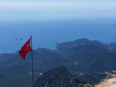 Türk bayrağı sisli deniz kıyısının arka planına karşı Tahtali Dağı 'nda dalgalanıyor. Akdeniz 'in manzarası. Olympos Teleferik, Tahtali 2365 metre, Kemer, Antalya.