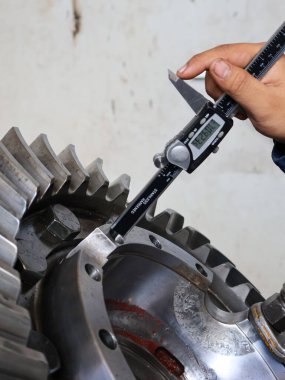 Dijital kalibreli bir aletle büyük, cilalı bir metal teçhizat montajının iç çapını ölçmek için bir insanın elinin yakın çekim görüntüsü. Görüntü kesin kalite kontrolüne odaklanır.