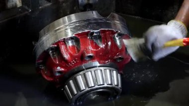 Bir işçinin eldivenli elleri, sıvı bir banyodan bilyeli büyük, karmaşık bir kırmızı ve gümüş metal bileşeni kaldırır. Bu ayrıntılı resim temizlik ya da bakım anını yakalar.