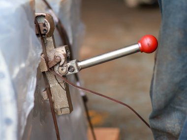 Bir paketi emniyete almak için kırmızı saplı elle bağlanma aracı, endüstriyel çalışma ve etkili paketleme süreçlerini vurguluyor.