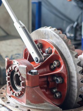 Bir tamirci diferansiyel başlık dişlilerinin vidalarını sıkmak için büyük bir tork anahtarı kullanır, endüstriyel onarım ve makine bakımını gösterir..