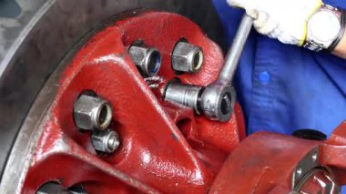 Kırmızı bir endüstriyel makinede vidaları sıkmak için soket anahtarı ya da kilit anahtarı kullanarak bakım ve onarım üzerine odaklanan bir tamircinin ellerinin yakın plan çekimi..