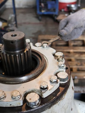 Ağır bir endüstriyel makinenin vidalarını sıkmak için İngiliz anahtarı ya da İngiliz anahtarı kullanan eldivenli bir elin yakın çekimi.