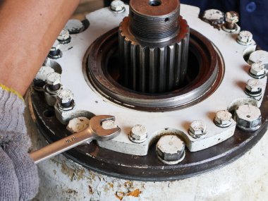 Ağır bir endüstriyel makinenin vidalarını sıkmak için İngiliz anahtarı ya da İngiliz anahtarı kullanan eldivenli bir elin yakın çekimi.