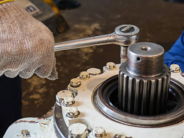 Diferansiyel kapağı vidaları sıkmak için soket anahtarı kullanan eldiven giymiş bir tamircinin yakın çekimi.