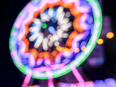 Dönme dolabın gece karanlığındaki renkli ışıkların güzel bir odak kaybı ya da bokeh etkisi, çeşitli renklerde, koyu bir arka plana karşı soyut, rüya gibi ışık çemberleri oluşturur..