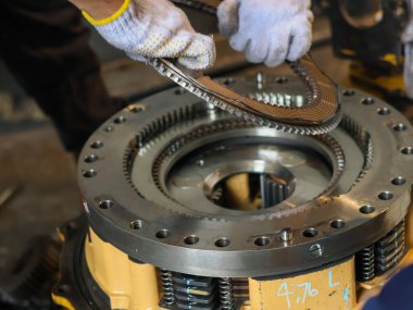 Eldivenli işçiler atölyede hassas aletlerle endüstriyel debriyaj mekanizması monte ediyorlar..