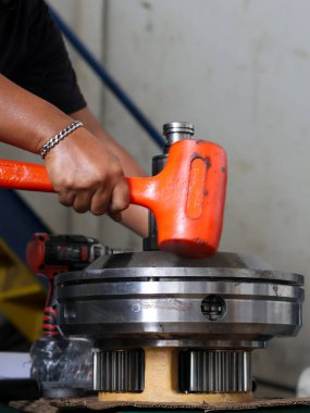 İşçi, atölyede hassas dişleri olan büyük metal teçhizat montajını ayarlamak için turuncu lastik çekiç veya yumuşak çekiç kullanıyor..