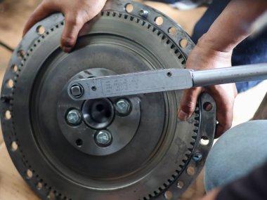 Mekanik ellerin, atölyede hassas cıvataları olan büyük metal çark üzerinde tork anahtarı kullanarak yakın plan görüntüsü.