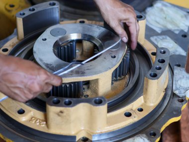 Fok pistonunu monte eden bir işçinin elleri, atölye ortamındaki karmaşık metal dişlilere ve parçalarına odaklanıyor..