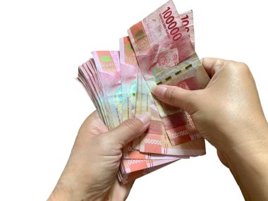 Close-up of hands counting Indonesian Rupiah banknotes. Focus on detail of red bills against white background. Great for finance, wealth, saving, banking, business, and economic concepts.