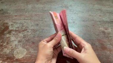 4K top view of hands quickly checking stack of Indonesian rupiah bills on rustic wood table. Perfect for finance, salary, savings, audit, transaction, and money themes.