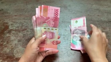 Hands carefully counting rupiah bills one by one on rustic surface. 4K sharp close-up, great for salary, savings, banking, economy, financial planning, and business themes.