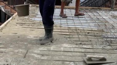 Endonezya-Eylül 07.2025-K görüntü inşaat işçisi çelik temelde ıslak çimento karışımı kullanıyor. Kapalı zemin açısı bot, alet ve takım çalışmasının detaylarını gösteriyor. inşaat, işgücü ve sanayi konsepti