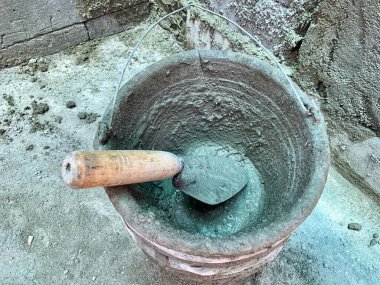 Close-up of wet cement mix in bucket with wooden trowel. Strong detail and texture, ideal for construction, renovation, masonry, repair, and industrial themes.